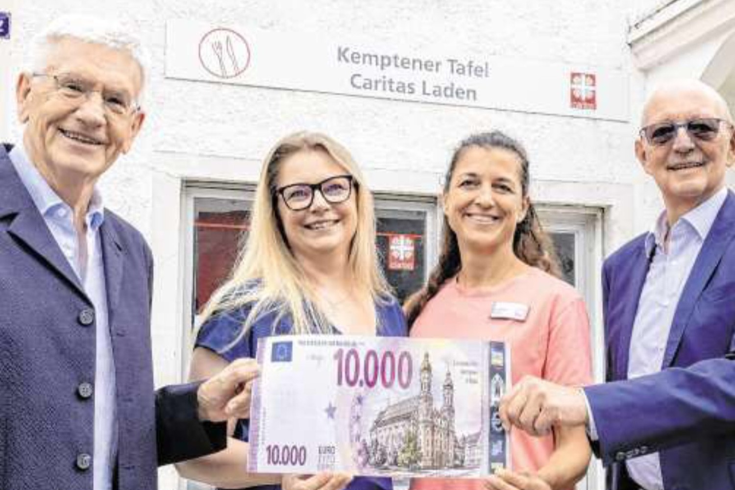 Vier Personen halten vor dem Kemptener Tafelladen einen symbolischen Scheck über 10.000 Euro in die Kamera.